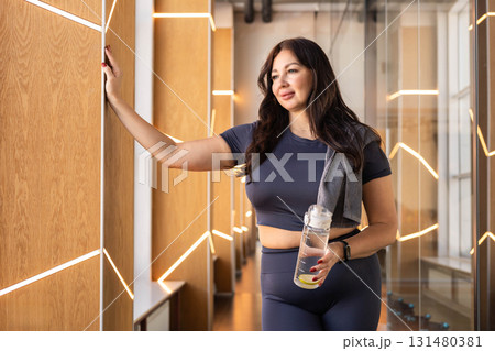 Fit woman holding lemon water and relaxing in gym after training session with confident look Fit woman holding lemon water and relaxing in gym after training session with confident look 131480381