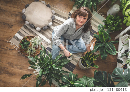 A young woman enjoys caring for flowers. Watering indoor plants and admiring them. 131480418
