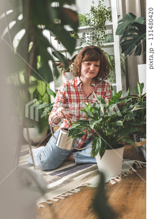 A young woman enjoys caring for flowers. Watering indoor plants and admiring them. A young woman enjoys caring for flowers. Watering indoor plants and admiring them. 131480420
