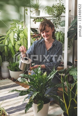 A young woman enjoys caring for flowers. Watering indoor plants and admiring them. A young woman enjoys caring for flowers. Watering indoor plants and admiring them. 131480422