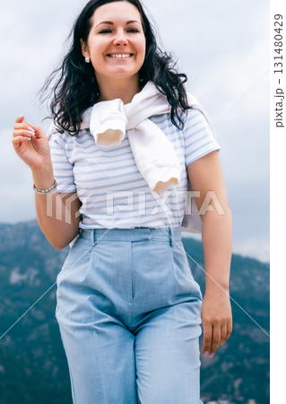 Smiling Woman in Striped Shirt and Light Blue Pants Enjoying Outdoor Walk on a Cloudy Day 131480429