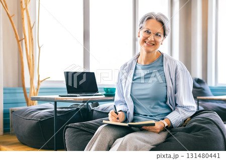 Smiling senior woman journaling with balance and mindfulness, enjoying vibrant lifestyle after 50 Smiling senior woman journaling with balance and mindfulness, enjoying vibrant lifestyle after 50 131480441