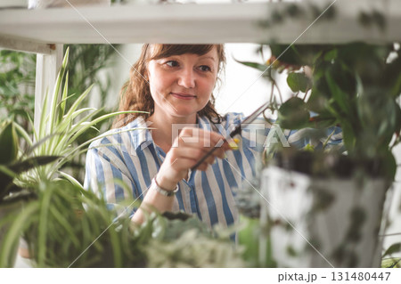 A young woman enjoys caring for flowers. Watering indoor plants and admiring them. 131480447