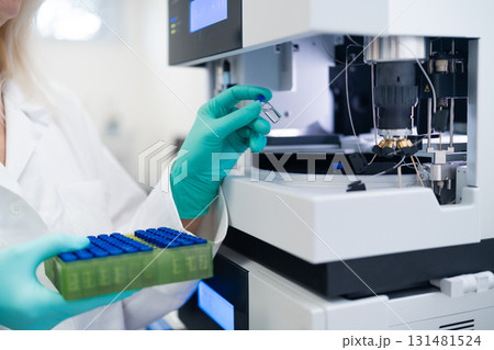 Scientist in rubber gloves carefully loading vial into autosampler for chemical, pharmaceutical, and clinical testing procedures Scientist in rubber gloves carefully loading vial into autosampler for chemical, pharmaceutical, and clinical testing procedures 131481524