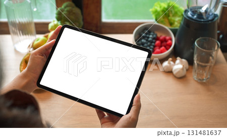 Hands holding digital tablet with blank screen in kitchen surrounded by healthy ingredients and blender Hands holding digital tablet with blank screen in kitchen surrounded by healthy ingredients and blender 131481637