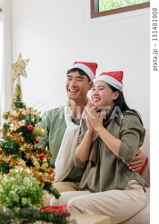 Christmas holiday brings happy couple love, joyful winter celebration at home, sharing warm smiles and laughter, wearing festive santa hats, near brightly decorated christmas tree. Christmas holiday brings happy couple love, joyful winter celebration at home, sharing warm smiles and laughter, wearing festive santa hats, near brightly decorated christmas tree. 131481908
