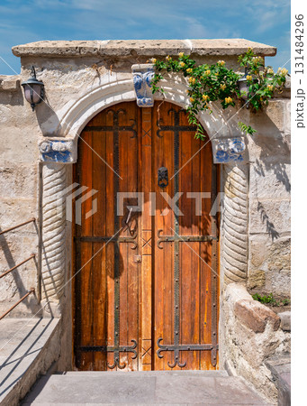 Ornate wooden door with face knocker, stone archway, blue painted details, lantern, and yellow flowers Ornate wooden door with face knocker, stone archway, blue painted details, lantern, and yellow flowers 131484296
