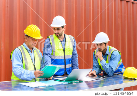 Group of container operators wearing helmets and safety vests meeting about logistics operations in container yards. Colleagues Talk About Logistics Operations 131484654