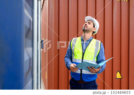 Foreman or Engineer wears white helmet and reflection shirt to control or check inventory details of containers box. Container loading cargo freight in import and export business logistic industry 131484655