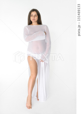 A sensual, gentle pregnant woman in transparent dress on white background. Waiting for baby to be born. Preparation of pregnancy. Maintaining an emotional state against of hormonal disruptions A sensual, gentle pregnant woman in transparent dress on white background. Waiting for baby to be born. Preparation of pregnancy. Maintaining an emotional state against of hormonal disruptions 131489133