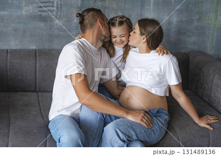 A laughing girl gets kisses from her father and pregnant mother. Loving parents. A happy family awaiting the birth of a baby A laughing girl gets kisses from her father and pregnant mother. Loving parents. A happy family awaiting the birth of a baby 131489136