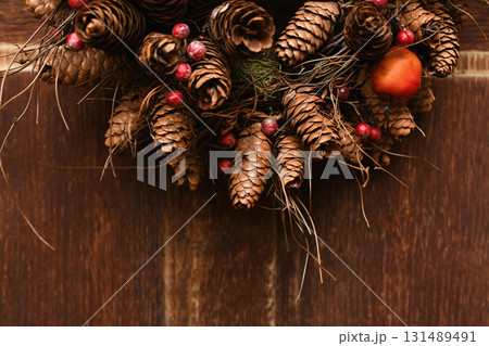 Christmas wreath in brown tones with pine cones, apples and berries on a wooden door Christmas wreath in brown tones with pine cones, apples and berries on a wooden door 131489491