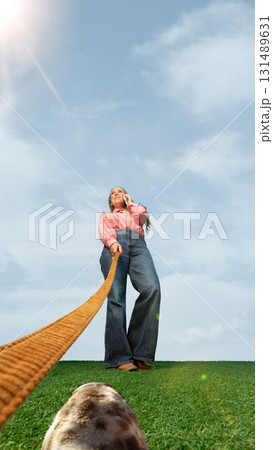Woman walking with long orange leash and talking on phone from dog ground view 131489631