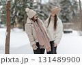 Two young women friends talking and laughing in a snowy park, dressed in warm winter clothing. Concept of friendship, happiness, and enjoying seasonal outdoor moments together. 131489900