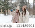 Two young woman taking selfie together in a snowy winter landscape, capturing joyful moments in a serene outdoor setting, copy space. Concept of friendship, technology and embracing seasonal beauty. 131489901