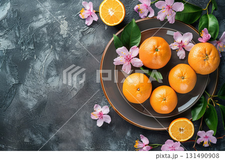 Five fresh oranges accompanied by delicate pink flowers and green leaves create a striking visual display on a dark background 131490908