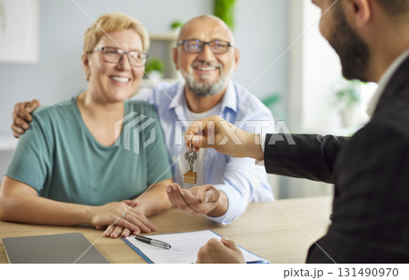 Realtor handing house keys to smiling senior couple after closing their purchase 131490970