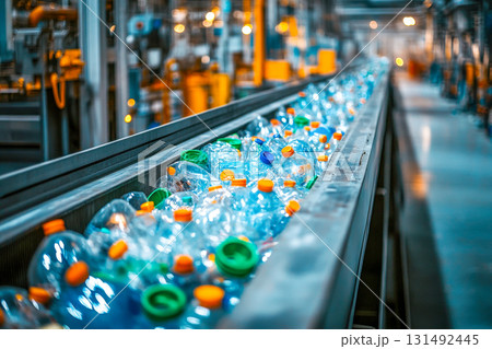 A conveyor belt transports colorful plastic bottles in a recycling plant. Workers nearby monitor the waste processing operations 131492445