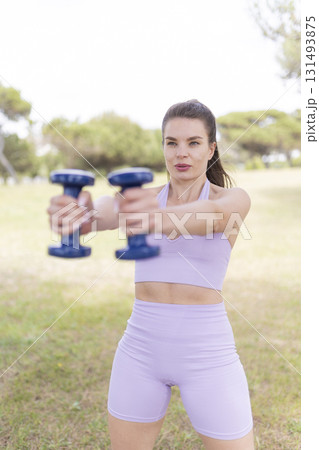 Woman training with dumbbells on grass for fitness Woman training with dumbbells on grass for fitness 131493875