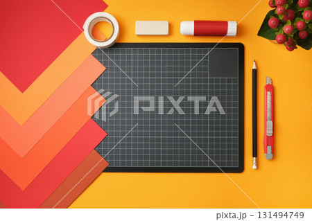 Workspace for paper crafts. Sheets of colored paper, cutting mat, pencil, knife, glue, and eraser on a yellow background. Copyspace Workspace for paper crafts. Sheets of colored paper, cutting mat, pencil, knife, glue, and eraser on a yellow background. Copyspace 131494749