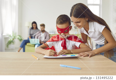 Happy little boy in superhero costume draws picture with help of his older sister. 131495222
