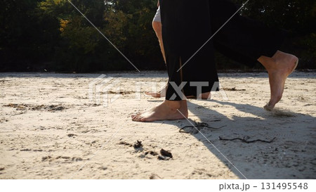 Male and female legs of pair walking on sandy beach. Bare feet of couple stepping along sand shore at sunny day. Lovers spending time together at resort. Concept of summer vacation or holiday 131495548