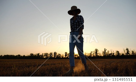 Adult agronomist in straw hat walking among barley plantation at dusk. Female farmer going through wheat meadow at sunset. Beautiful scenic landscape. Concept of agricultural business. Slow motion Adult agronomist in straw hat walking among barley plantation at dusk. Female farmer going through wheat meadow at sunset. Beautiful scenic landscape. Concept of agricultural business. Slow motion 131495551