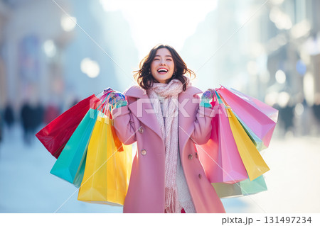 冬のショッピングを楽しむ笑顔の女性｜カラフルな紙袋と光に包まれた華やかな街中で 131497234