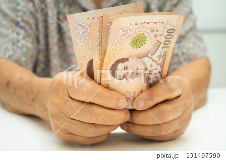 Asian elder senior woman patient holding Thai banknotes money in her hand, Cost of living and medical care. Asian elder senior woman patient holding Thai banknotes money in her hand, Cost of living and medical care. 131497590