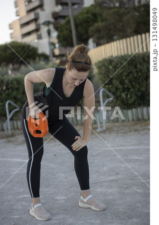 Woman exercising outdoors with weight plate feeling knee discomfort 131498049