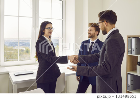 Business people standing in office making deal. Man shaking hands with woman finishing meeting. 131498653