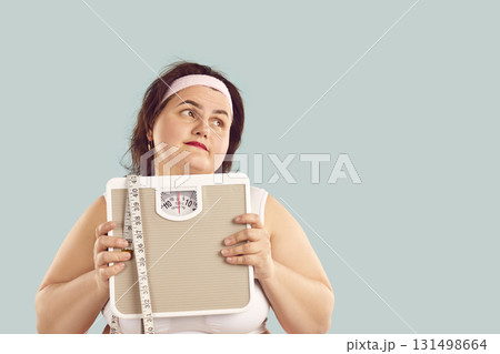 Fat woman holding scales, looking at copy space background, and dreaming of perfect body 131498664