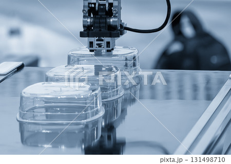 Close up scene material handling process the food container by robotic system from injection machine in the light blue scene. 131498710
