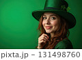 Woman wearing a green hat and green dress on green background. She is smiling and looking at the 131498760
