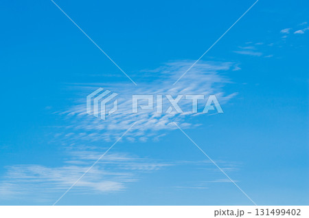 Background photo of a blue sky with wavy white clouds disintegrating under the influence of wind currents. Atmospheric phenomena in the upper layers. Natural surroundings 131499402