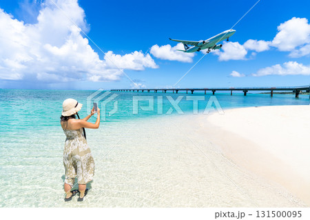 エメラルドのビーチで飛行機の着陸をスマホ撮影するワンピース姿の若い女性 131500095