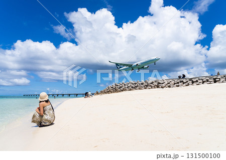 エメラルドのビーチで飛行機を見上げるワンピース姿の若い女性 131500100