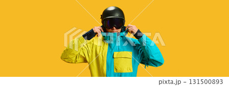 Skier adjusting helmet and goggles in yellow studio wearing ski jacket 131500893