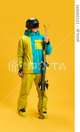 Skier holding skis upright in bright yellow studio with protective helmet and goggles Skier holding skis upright in bright yellow studio with protective helmet and goggles 131500895