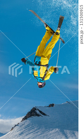 Male skier upside down performing backflip trick over snowy mountain slope 131500915