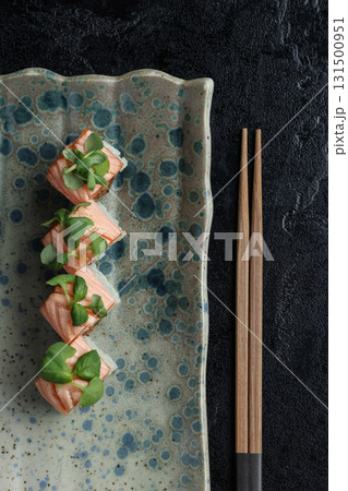 A beautifully textured ceramic plate showcases delicate salmon sushi cubes topped with fresh green leaves. A beautifully textured ceramic plate showcases delicate salmon sushi cubes topped with fresh green leaves. 131500951