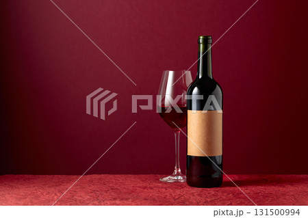 Bottle with old empty label and glass of red wine on a red background. Bottle with old empty label and glass of red wine on a red background. 131500994