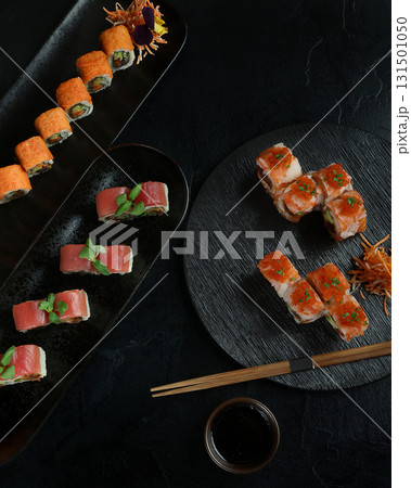 An elegant sushi platter featuring a variety of rolls on black plates 131501050