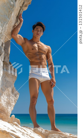 Fit Asian man in swim shorts standing on a tropical beach with a clear blue sky 131501412