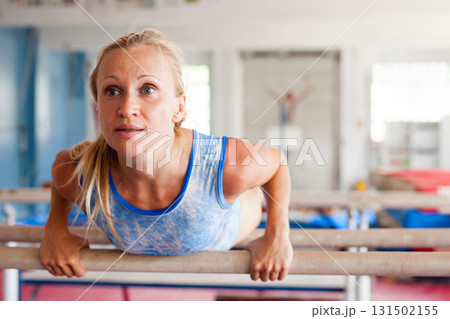 Woman gymnast performs complex acrobatic exercise on parallel bars in gym Woman gymnast performs complex acrobatic exercise on parallel bars in gym 131502155