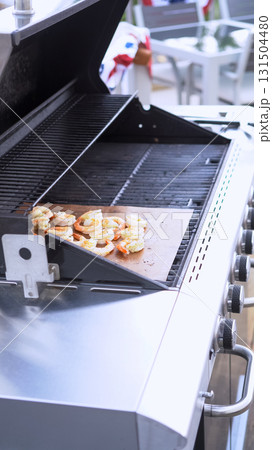 An open outdoor gas grill reveals bread toasting on a metal tray inside. The grill setup is clean and modern, emphasizing outdoor cooking and food preparation. 131504480