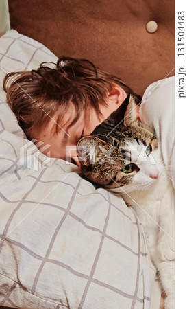 Teenage boy and a cat. Handsome guy hugs his cat while sitting on the couch. teenage boy on the couch is petting his cat. Vertical 131504483