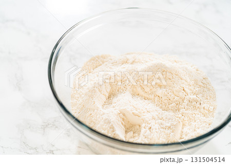 A large glass bowl filled with flour, prepped for the next batch of the Classic Red Gingerbread Dough. Flour provides the structure to the dough, balancing the moisture from the molasses and eggs. A large glass bowl filled with flour, prepped for the next batch of the Classic Red Gingerbread Dough. Flour provides the structure to the dough, balancing the moisture from the molasses and eggs. 131504514