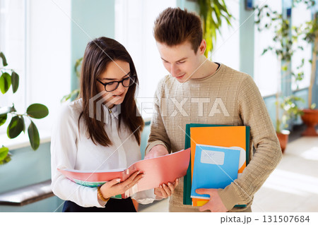 Two young cheerful students working together during break, happy to express personal points of view towards the topic. Hard-working learners discussing some problem in corridor of university 131507684