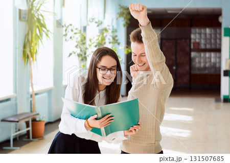 Two young cheerful students working together during break. Hard-working learners are very glad to receive excellent marks for tests or exams in the corridor of university 131507685